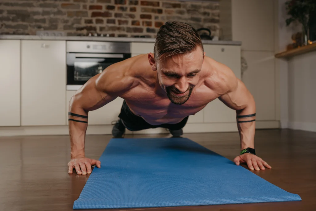 happy-muscular-man-with-beard-is-doing-pushups-blue-yoga-mat-his-apartment-evening